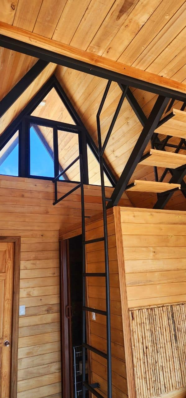 Architectural interior of A-frame cabin with metal staircase and exposed beams, part of your upscale stay