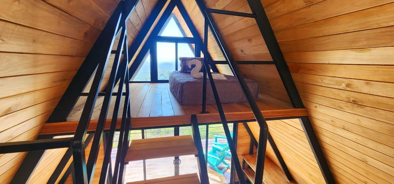 View of the upper loft in A-frame cabin with bed and triangular window overlooking Blue Zone mountains