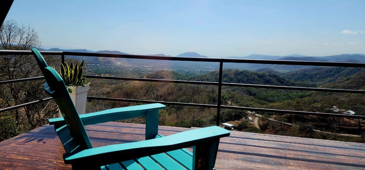 Turquoise Adirondack chair on wooden terrace with panoramic valley view, ideal for a relaxing vacation stay