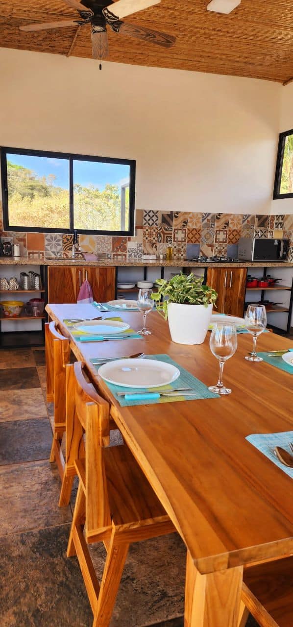 Wooden dining table with chairs and kitchen with artisanal tile backsplash at Bluesky Lodge