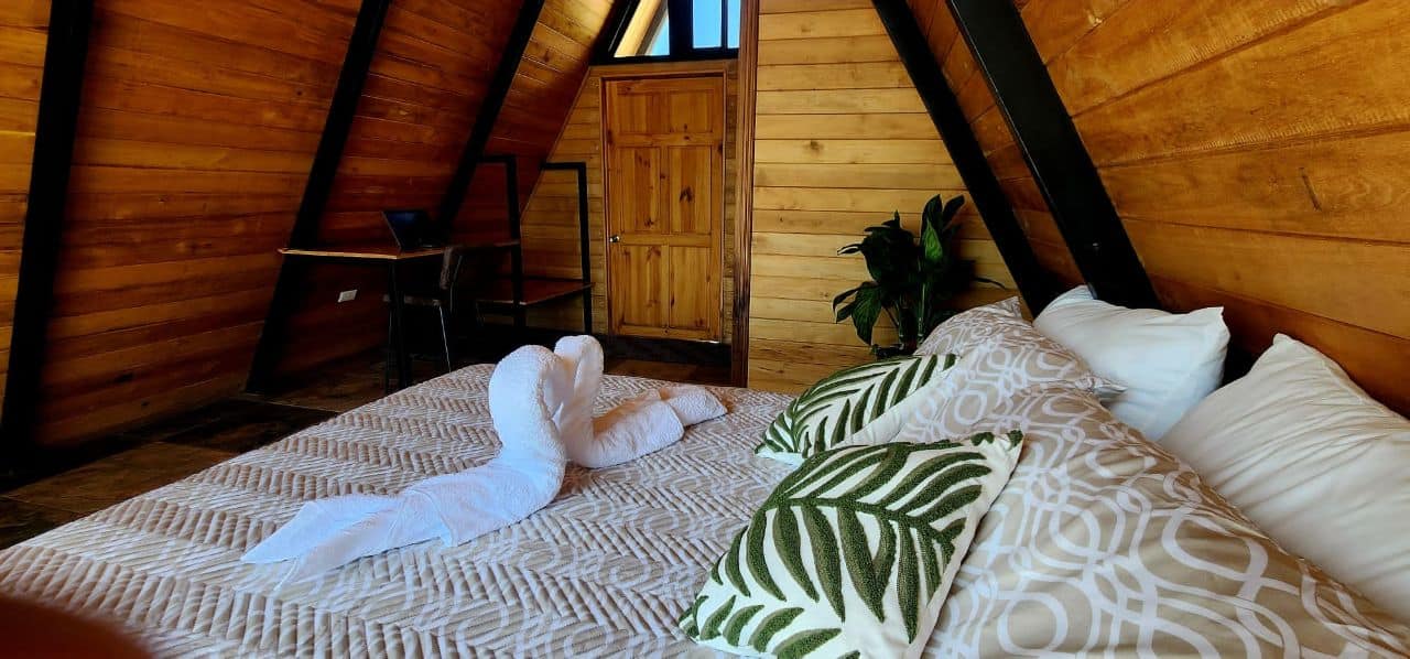 Cozy A-frame bedroom with wooden walls, decorative towels, and plants, offering an exclusive vacation stay experience