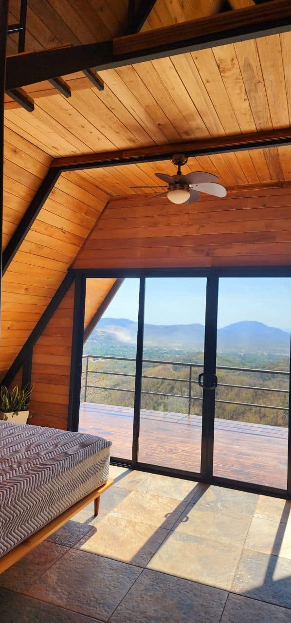 Interior of A-frame cabin with wooden ceiling, fan, and mountain view, offering luxury comfort for your stay