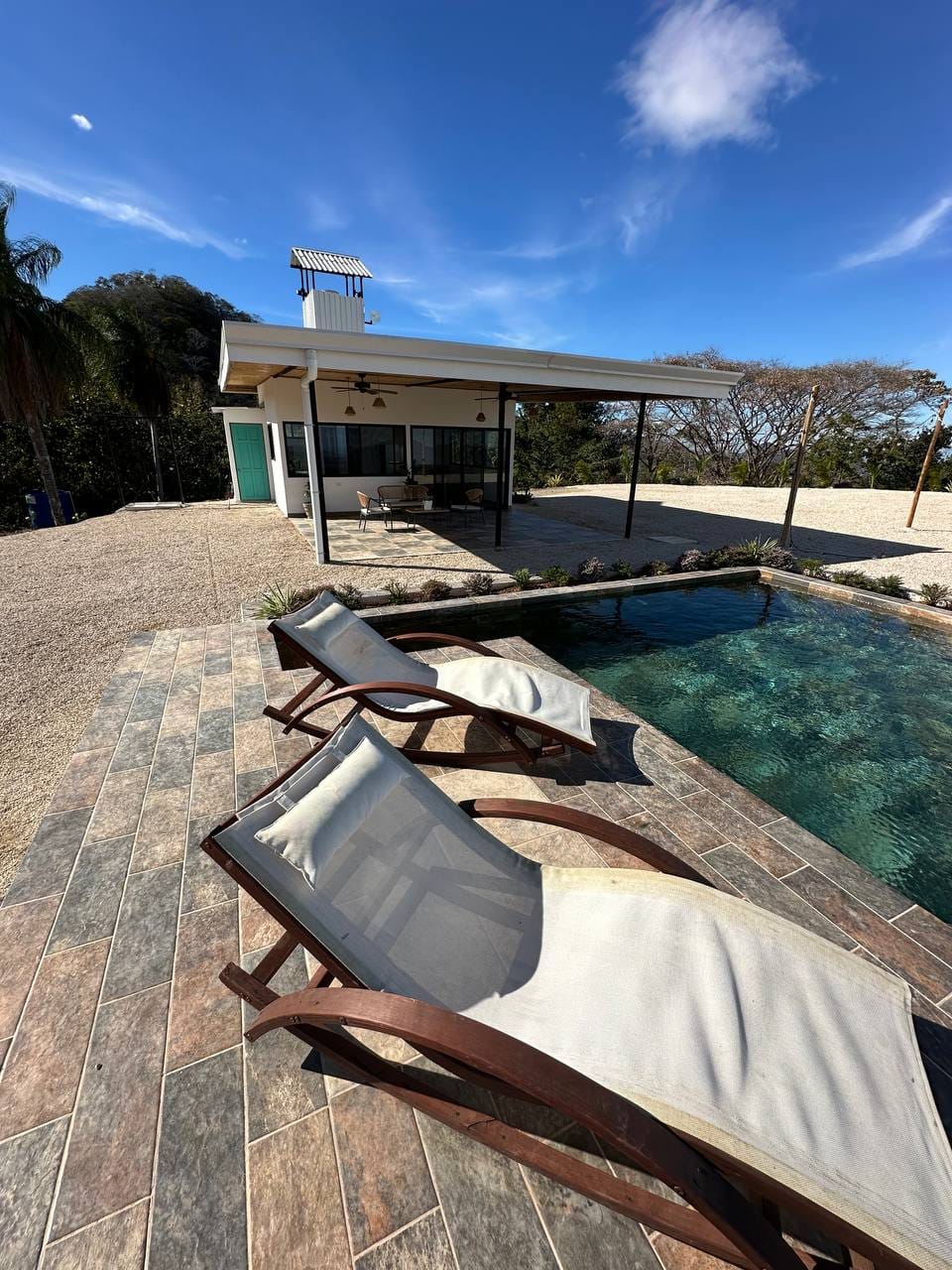 Pool area with lounge chairs and view of the main lodge under blue sky, an exclusive vacation spot